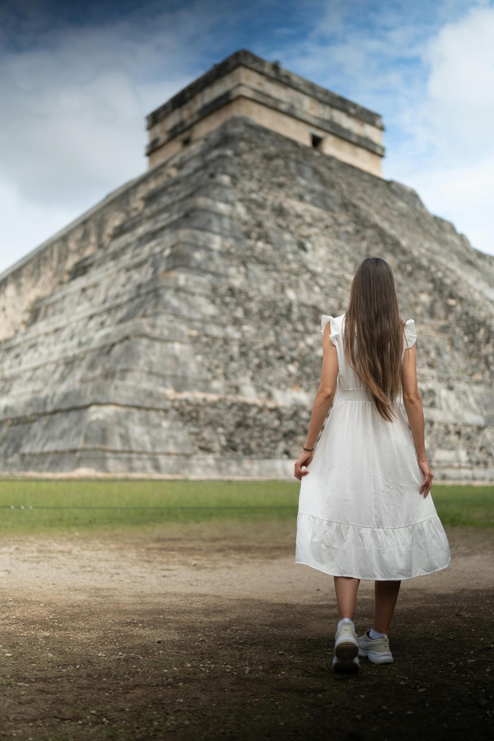 A woman in a white dress stands facing the Chichen Itza pyramid, Mexico.